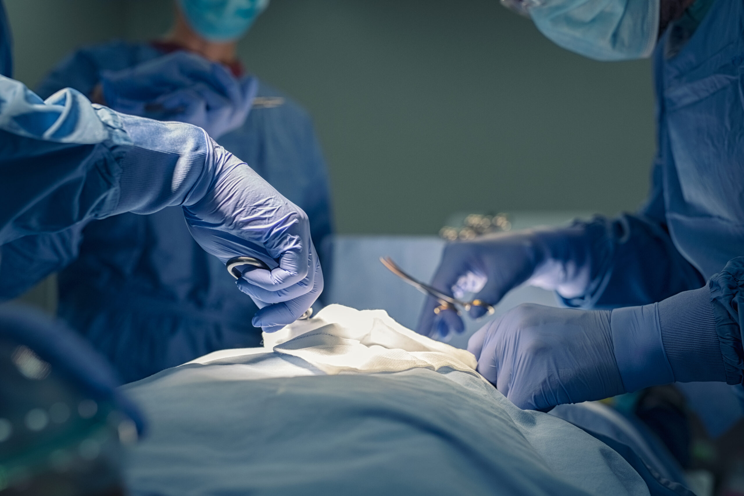 Close up of hands of medical team performing surgery at operation theater. Group of surgeons at work in operating theatre saving patient life. Detail of group of doctors hands and healthcare workers holding medical instruments and working in operating room.